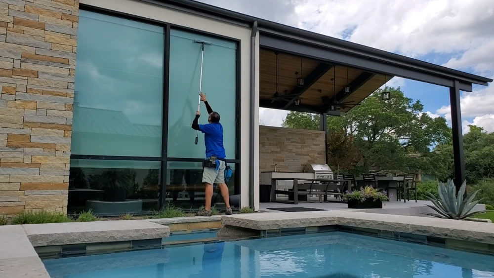 Professional window cleaner using a water-fed pole to clean exterior windows on a modern San Clemente, CA home